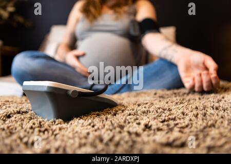 Una vista selettiva di fuoco di una donna gravida vicino al lavoro, la mano di appoggio sui calci di sensibilità del tummy, controllo della pressione sanguigna sullo sfigmomanometro Foto Stock