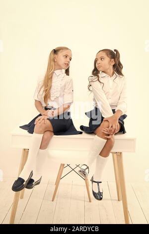 Tenetevi pronti per il ritorno a scuola. Scuola elementare di alunni in uniforme formale seduta sul tavolo. Poco studentesse di parlare in aula scolastica. Bambini piccoli godendo di scuola tempo di pausa. Foto Stock