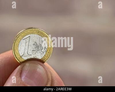 mano maschile che tiene una moneta di un euro su sfondo sfocato con spazio copia Foto Stock