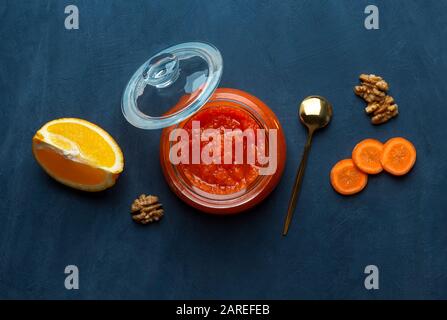 Un vaso di marmellata di carote e arancione su uno sfondo blu scuro. Vista dall'alto, spazio di copia Foto Stock