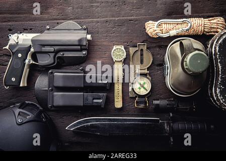 Equipaggiamento tattico militare per la partenza. Assortimento di attrezzi da trekking di sopravvivenza su sfondo di legno. Vista dall'alto - effetto filtro granella a film vintage st Foto Stock