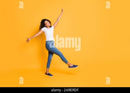 Foto a tutta lunghezza del corpo girata di allegra ragazza ballante graziosa pazzesca che indossa la t-shirt bianca jeans scarpe denim isolato su colore vivo Foto Stock