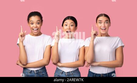 Tre Millennial Girls Pointing Finger Up Standing, Pink Background, Panorama Foto Stock