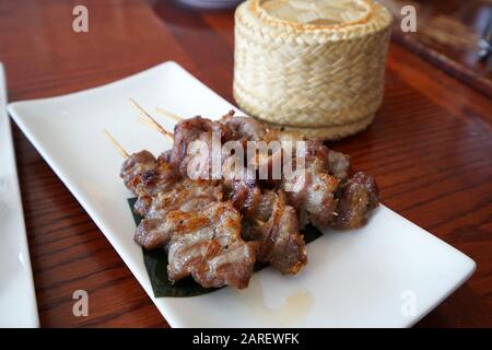 Spiedini di maiale barbecue serviti con un cesto di legno di riso appiccicoso, ricetta tailandese Foto Stock