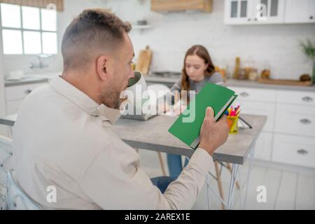 Uomo barbuto dai capelli corti che tiene un libro verde Foto Stock
