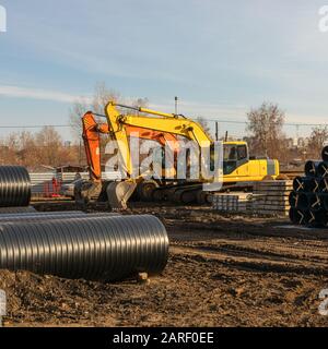 Due escavatore giallo in cantiere contro cielo blu. Costruzione di condotte per l'approvvigionamento idrico domestico. Foto Stock