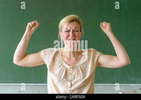 Arrabbiato insegnante frustrato di scuola che getta un tantrum temper che perfora l'aria con i suoi pugni con un aspetto di furia davanti ad un chalkboard Foto Stock