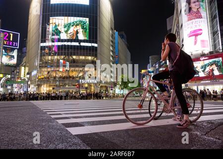 Tokyo, Giappone - 27 giugno 2016: Ciclisti e pedoni attendono di attraversare la strada all'incrocio di Shibuya Crossing. Ripresa serale a Tokyo, Jap Foto Stock