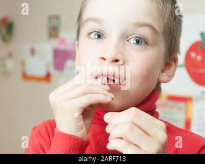 Ragazzo holding perso i denti decidui contro il suo disegno sulla parete Foto Stock