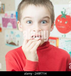 Ragazzo holding perso i denti decidui contro il suo disegno sulla parete Foto Stock