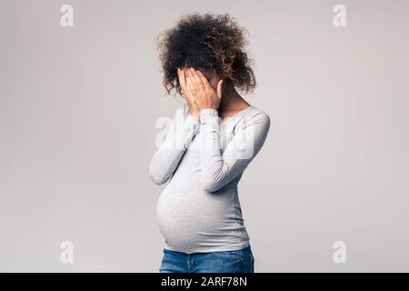 Depressione durante la gravidanza. Afro donna che copre il viso con le mani Foto Stock