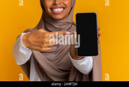 Unirriconoscibile Afro Woman In Hijab Che Punta Allo Smartphone Con Schermo Nero Foto Stock