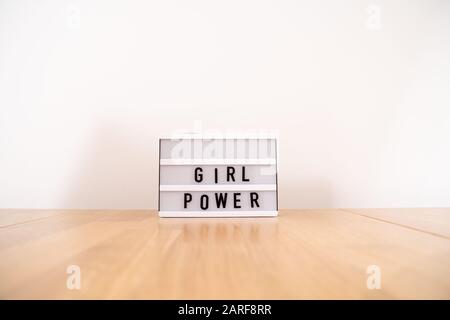 Testo alimentazione ragazza sulla scatola luminosa. Vista laterale sul tavolo in legno. Parità di genere Foto Stock