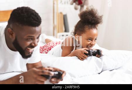 Felice padre e figlia di famiglia nera che gioca a videogame in camera da letto Foto Stock