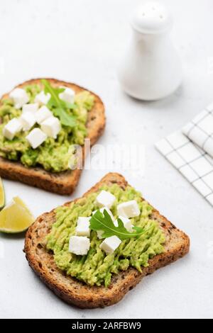 Avocado e formaggio feta pane tostato integrale. Sano spuntino vegetariano o colazione su sfondo bianco Foto Stock