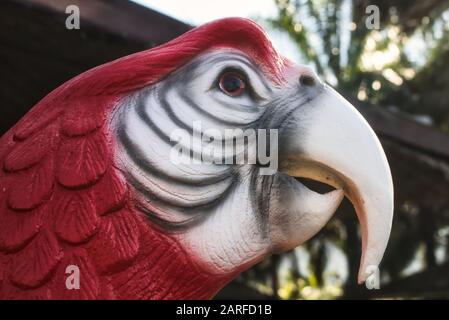 Questa foto unica mostra una testa di una statua di pappagallo in rosso e bianco in piedi in un giardino. Potete vedere i dettagli molto bene. Foto Stock