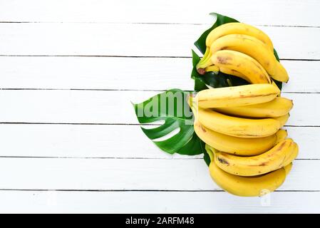 Banana con foglie verdi su un tavolo di legno bianco. Frutti Tropicali. Vista dall'alto. Spazio libero di copia. Foto Stock