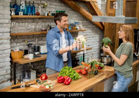 Giovane coppia trendy peeling e taglio verdure dal mercato in cucina rustica Foto Stock