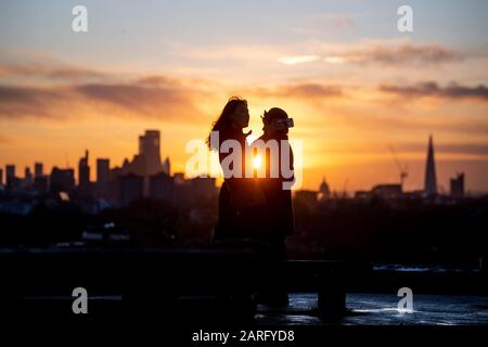 Persone su Primrose Hill guardano il sole sorgere su Londra. Foto Stock