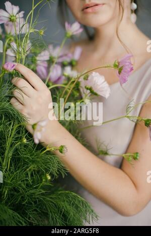 Una giovane Bella ragazza in un abito rosa tenendo un Bouquet Delicato di fiori su uno sfondo grigio Foto Stock