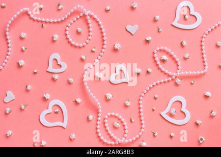 Composizione di primavera con fiori, cuori e perle su uno sfondo rosa Foto Stock