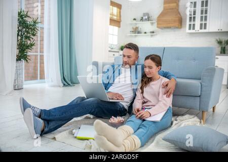 Papà e figlia seduti sul pavimento guardando un computer portatile. Foto Stock