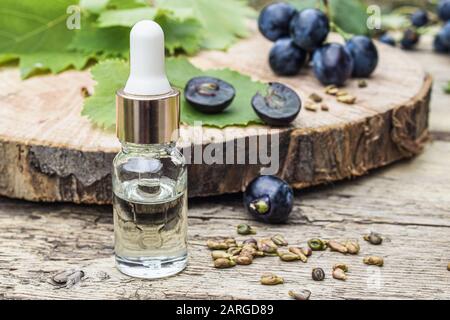 Olio di semi d'uva in vaso di vetro e uve fresche su vecchi pannelli di legno. Il concetto di prodotti SPA, Bio, Eco. Foto Stock