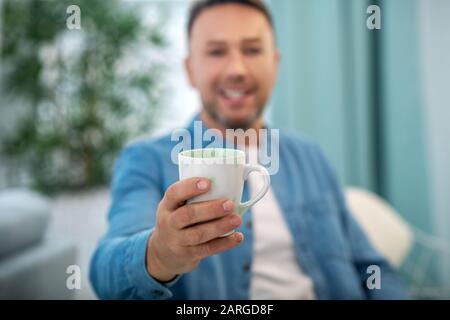 Tazza di tè nella mano distesa dell'uomo. Foto Stock