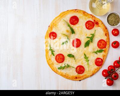Pizza calda italiana margherita fatta in casa con mozzarella e pomodori su un tavolo di legno bianco, vista dall'alto Foto Stock