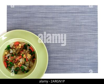 Zuppa di verdure semplice in ciotola verde, placemat grigio, vista dall'alto, spazio di copia Foto Stock