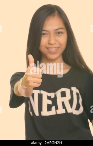 Studio shot di giovani felici Asian teenage nerd ragazza sorridente e dando un pollice alzato con focus sul pollice Foto Stock