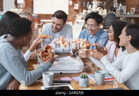 Un team di lavoro positivo che mangia la pizza in ufficio Foto Stock