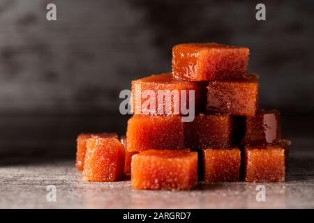 Primo piano di alcuni cubetti di mela cotogna formaggio su grigio di una tavola in legno rustico, contro uno sfondo scuro con qualche spazio vuoto sulla parte superiore Foto Stock