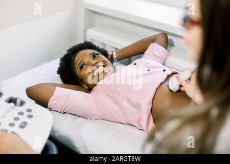 Felice sorridente donna afroamericana incinta ottenere ultrasuoni dal medico nel moderno centro medico Foto Stock