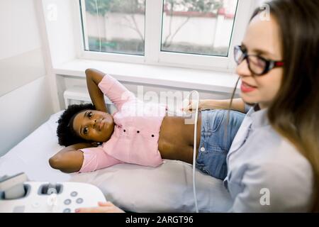 Giovane medico professionista che fa un ecografo dei reni di giovane donna africana paziente in clinica medica moderna Foto Stock