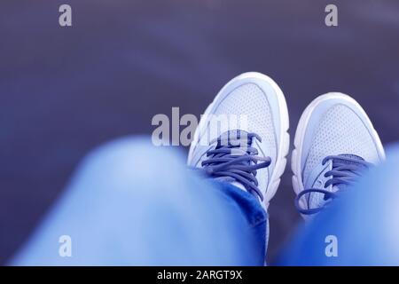 Gambe appese sull'acqua da parapetto, jeans blu, sneakers grigie e bianche, look per la prima persona Foto Stock