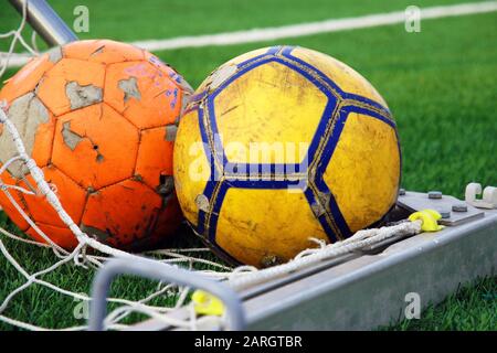 Due palloni da calcio stracciati che si trovano nell'angolo della meta contro il campo di calcio verde Foto Stock