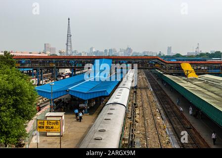 New Delhi stazione ferroviaria con tracce e treni, lo skyline di Connaught Place nella distanza nebulosa Foto Stock