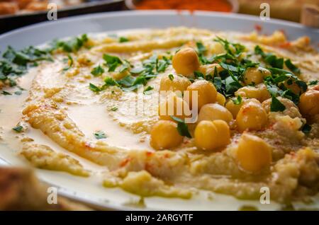 Vista sul closeup all'Hummus sormontato da olio di oliva di fagioli e foglie di coriandolo verde sul tavolo da cucina Foto Stock