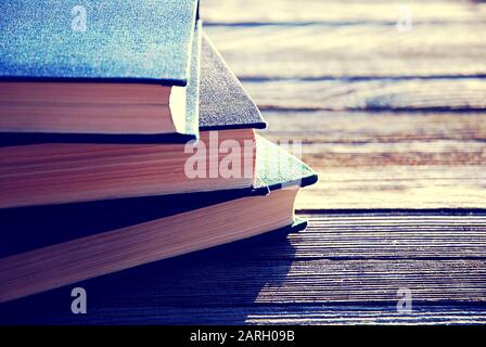 Stack di tre vecchi libri in retroilluminazione su tavolo in legno, fuoco selettivo Foto Stock