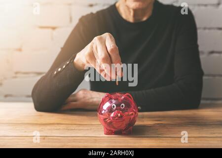 previdenza - donna senior che mette la moneta in una banca piggy Foto Stock