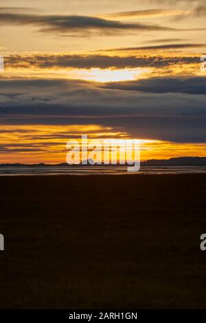 Dawn sulla costa Northumbrian, guardando attraverso le tonde mudflats verso Bamburgh Castle Inghilterra, Regno Unito, GB. Foto Stock