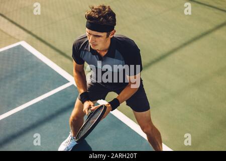 Giocatore di tennis professionista che gioca una partita sul campo duro. Sportivo caucasico in piedi sulla linea di base pronto a colpire la palla sul campo da tennis. Foto Stock