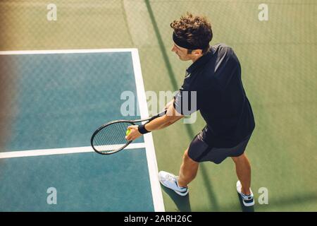 Vista dall'alto di un giovane giocatore di tennis con racket pronto a servire una palla da tennis. Giocatore professionista in piedi al basale che tiene la racchetta da tennis e. Foto Stock