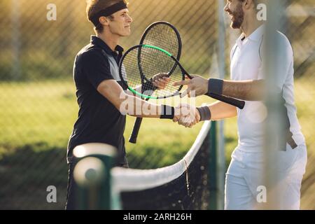 Giocatori professionisti di tennis che scuotono le mani in rete. Due sportivi che scuotono le mani sulla rete dopo la partita. Foto Stock