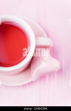 Frutta tè rosso e cuore di ceramica rosa su sfondo rosa pallido, copia spazio Foto Stock