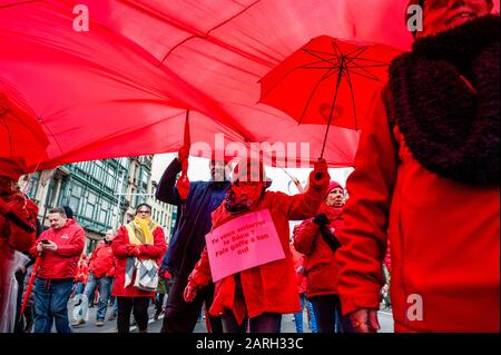 Una donna và sotto un'enorme bandiera rossa mentre tiene un ombrello rosso durante la manifestazione a Bruxelles. Il sindacato socialista ABVV ha organizzato una manifestazione nazionale per una sicurezza sociale forte e giustamente finanziata. Migliaia di persone si sono radunate intorno alla stazione settentrionale per combattere il rischio di un deficit di sicurezza sociale di 6,4 miliardi di euro entro il 2024 a causa del sottofinanziamento. La gente stava tenendo gli ombrelli rossi come simbolo di protezione. Foto Stock