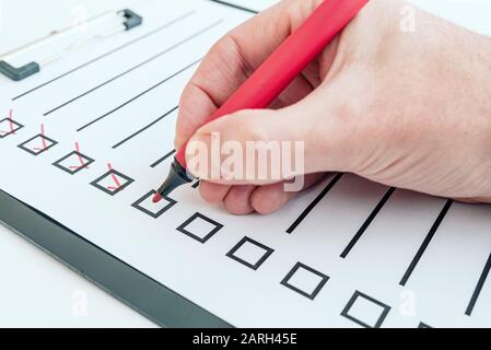 primo piano della mano che tiene la penna rossa che spunta fuori dalla lista di controllo o dall'elenco delle cose da fare negli appunti Foto Stock