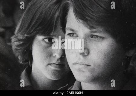 Fine anni '70 nero e bianco annata fotografia di un adolescente sussurrando ad un altro teen sospetto Foto Stock