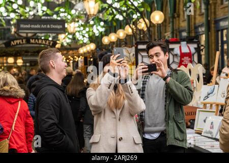 Londra / Regno Unito - 24 novembre 2019: Giovani uomini che fotografano decorazioni natalizie nel mercato Apple di Covent Garden, Londra, Regno Unito Foto Stock